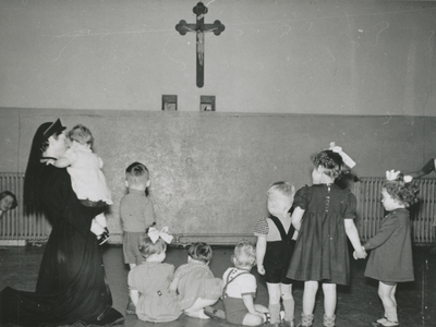 876972 Afbeelding van een geknielde Zuster Augustines met een groepje kleuters in de sport- en ontspanningszaal in het ...